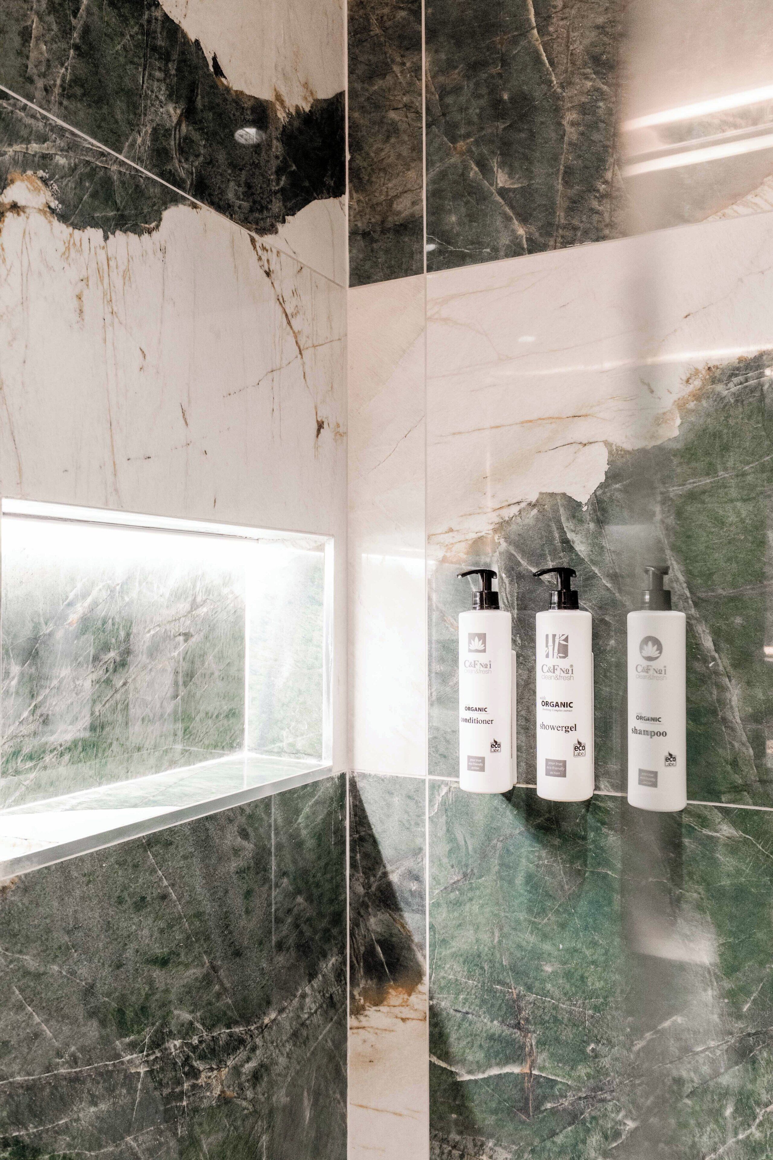Bagno con pareti in marmo, una finestra e tre prodotti di bellezza naturali.