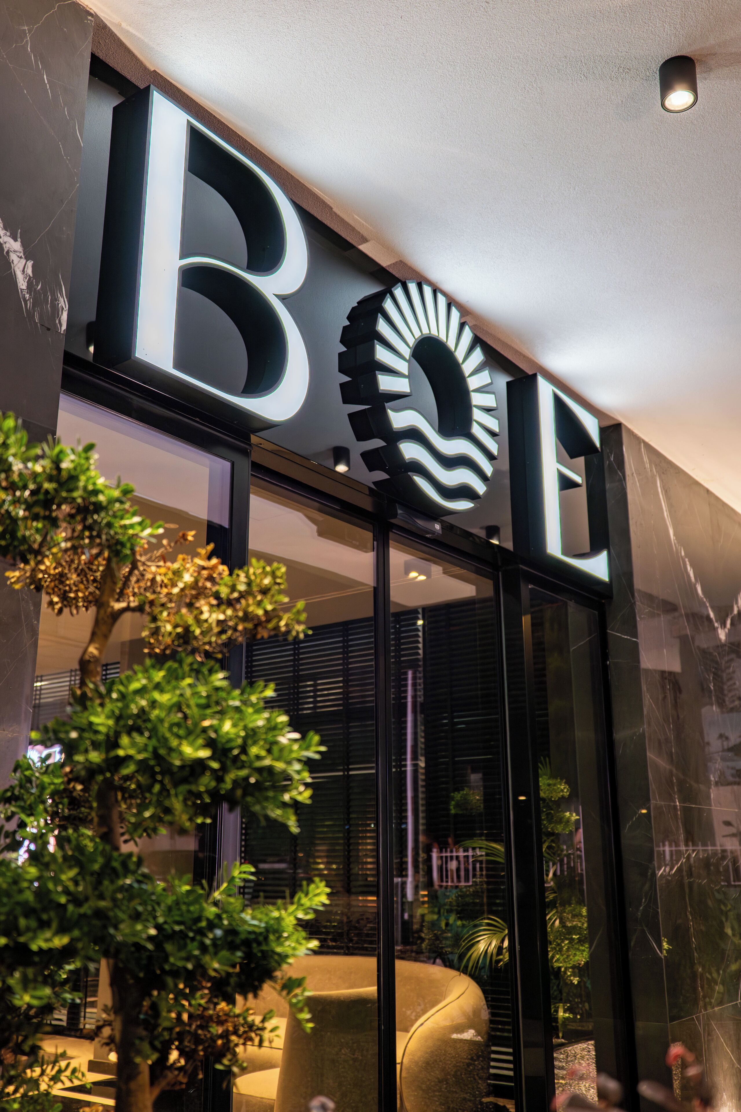 Une façade moderne avec une enseigne « BOE » bien visible, une entrée en verre et un arbre bien entretenu devant le bâtiment.