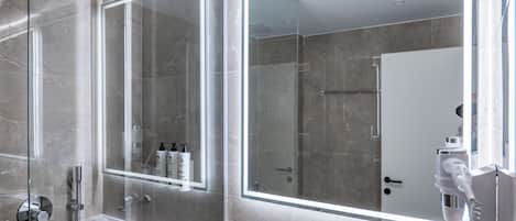 Een moderne badkamer met een douchecabine van glas, een witte wastafel en twee spiegels met ingebouwde verlichting.