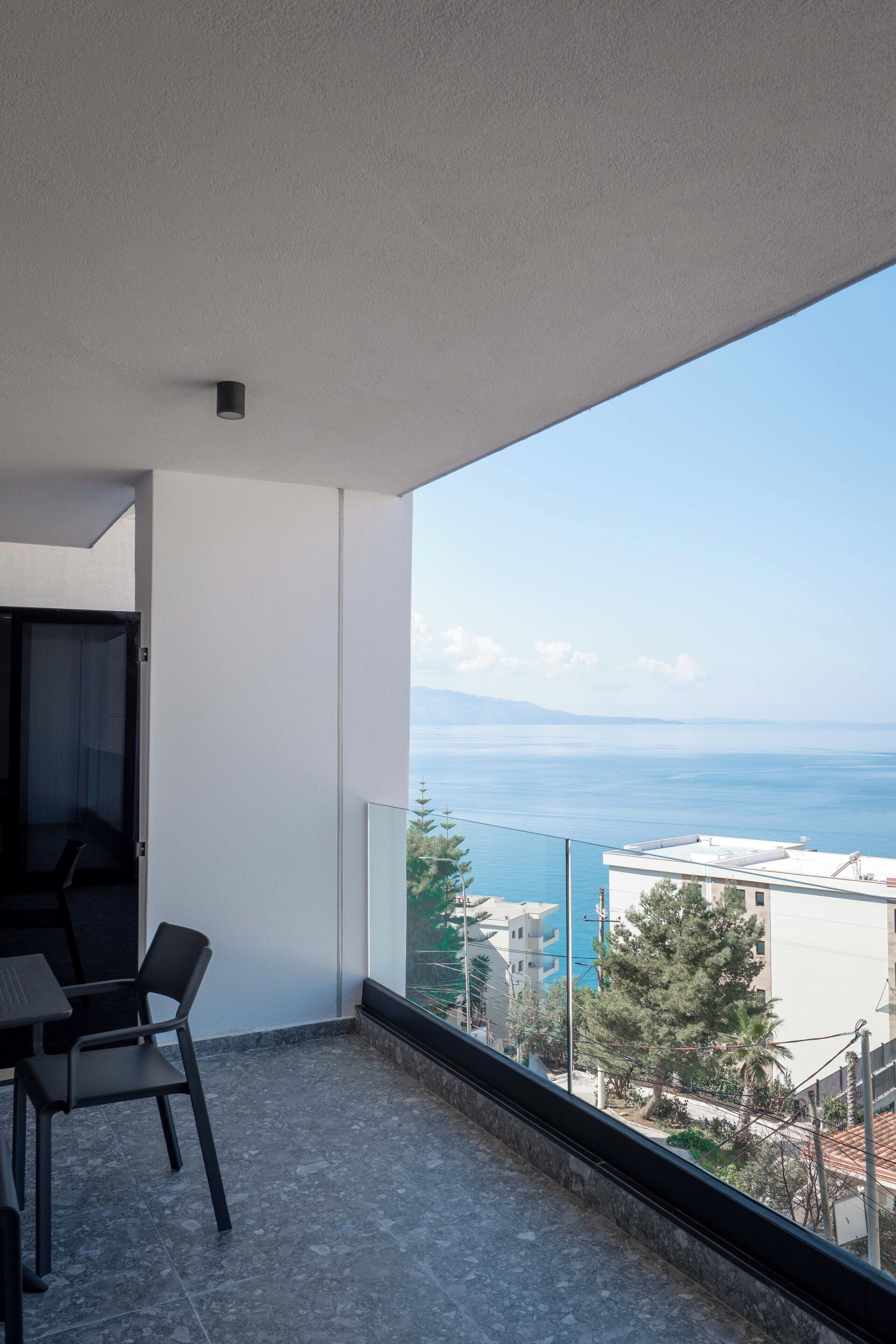 A balcony with a view of the sea, a table with chairs, and a door.