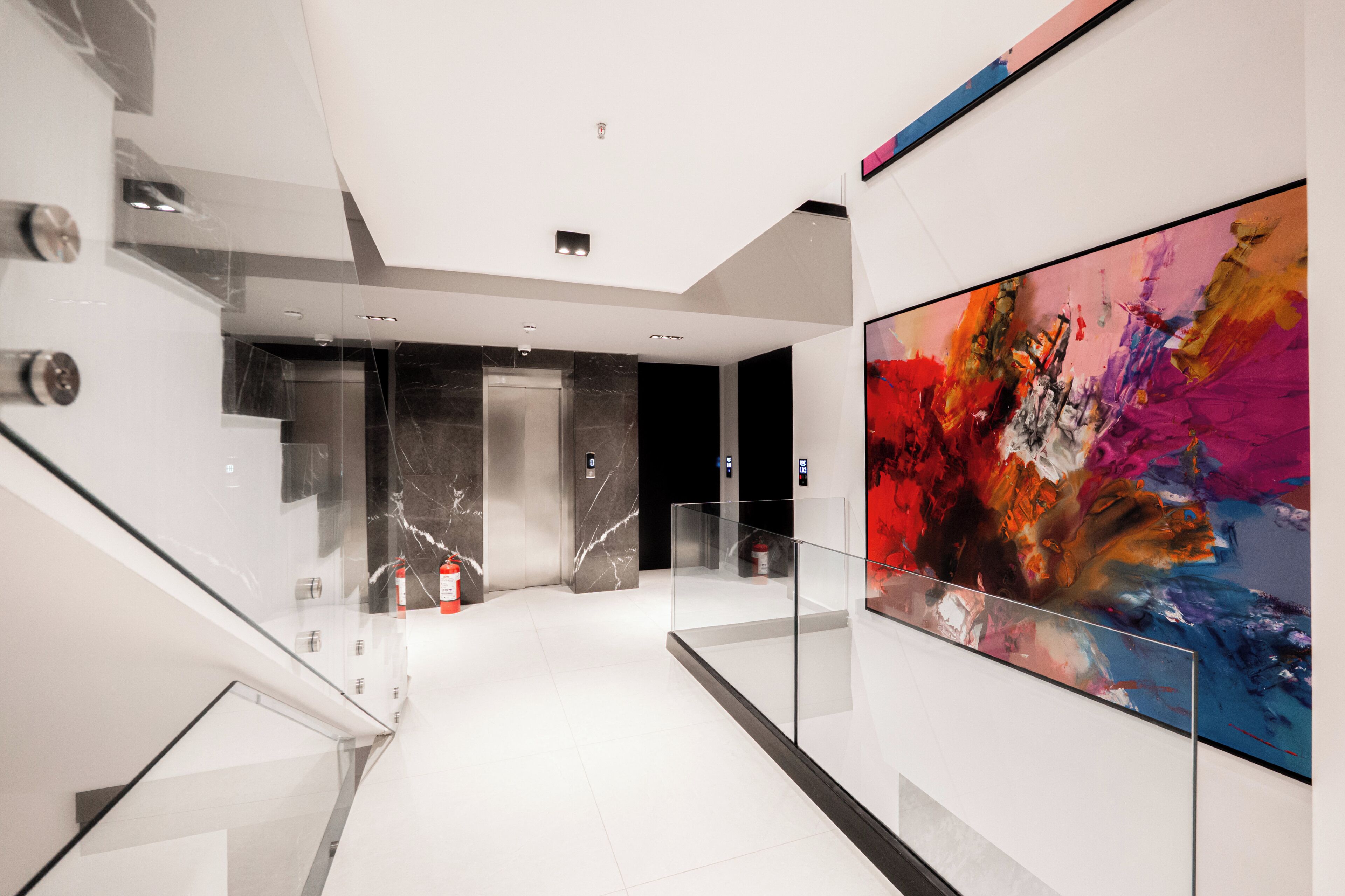 Un interior moderno con barandilla de vidrio, un cuadro abstracto grande y una escalera de mármol.