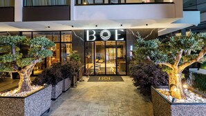 Ein Hotel mit moderner Gestaltung, das eine große Glasfassade, einen gut beleuchteten Eingangsbereich und einen einladenden Außenbereich mit Topfpflanzen bietet.
