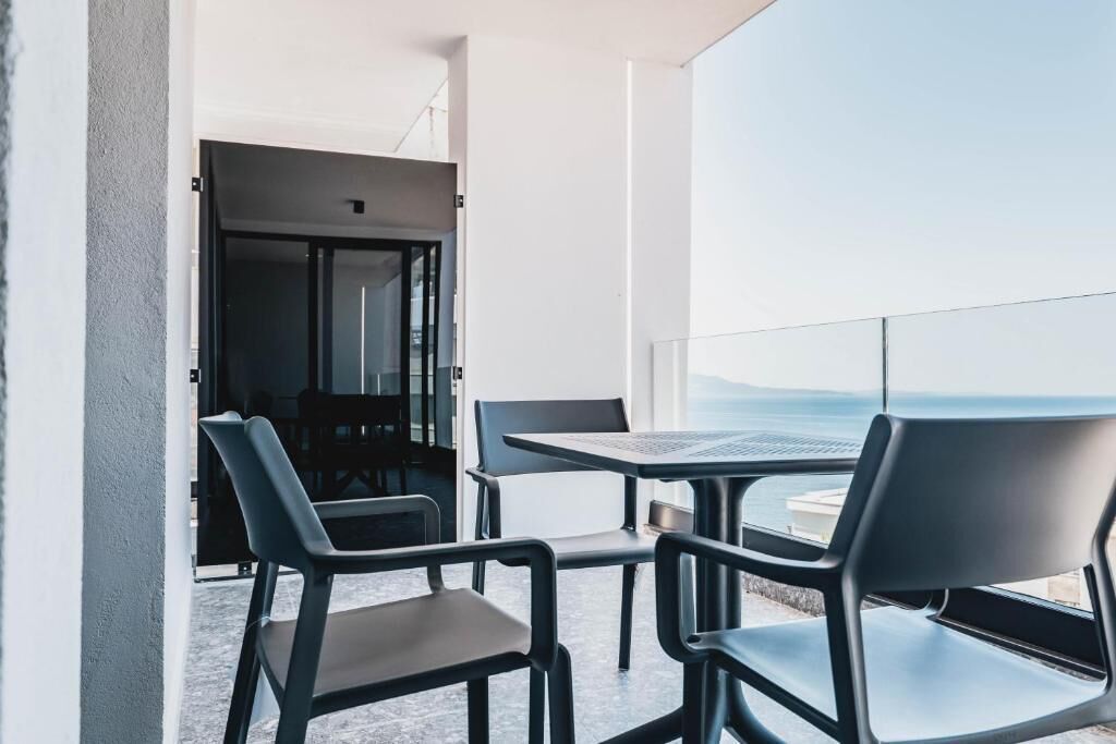 A balcony with a table and chairs, a view of the sea, and a door leading to an interior space.