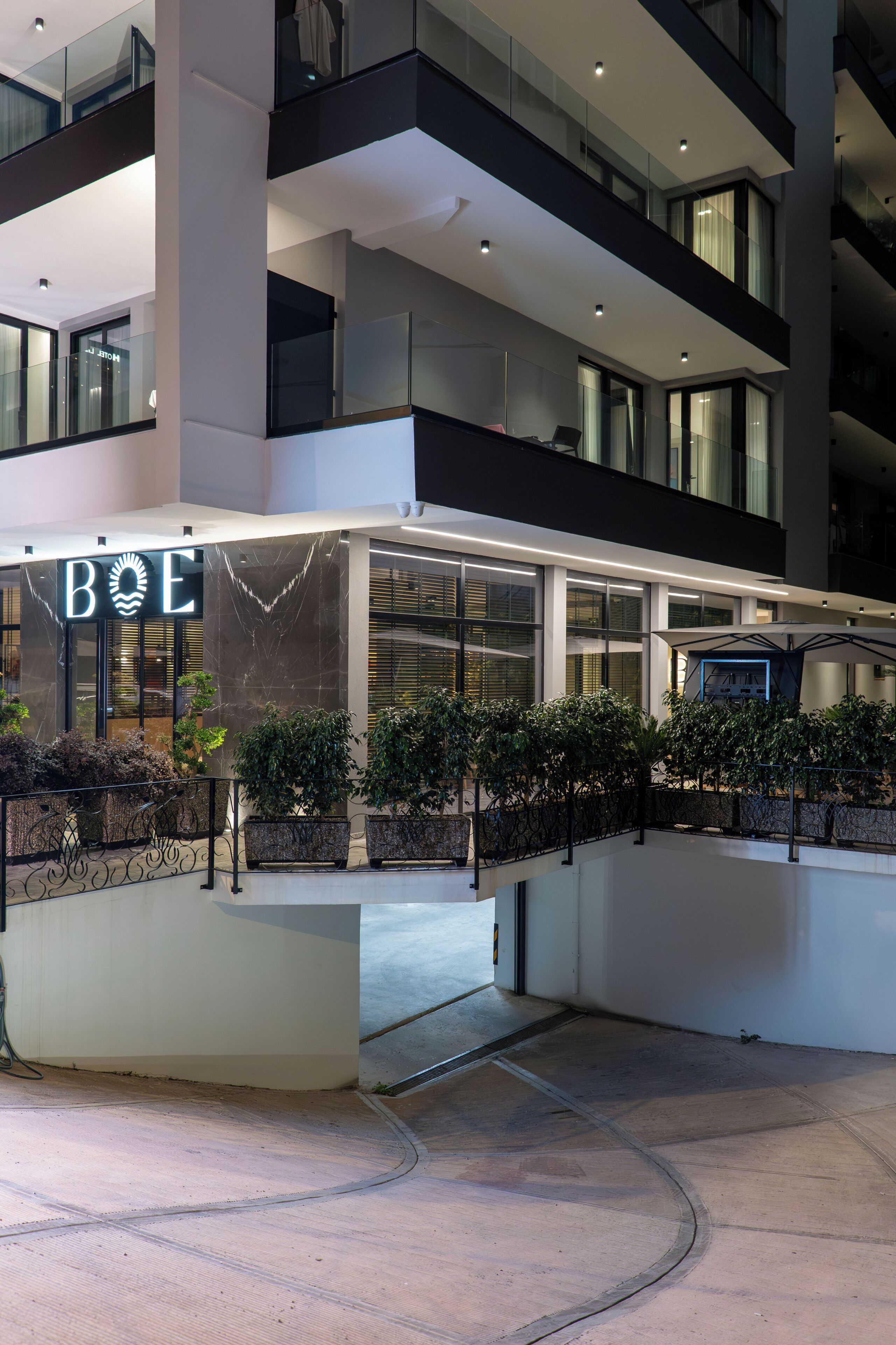 Un edificio moderno con fachada de vidrio, un cartel que dice 'BOE' y asientos exteriores con plantas.