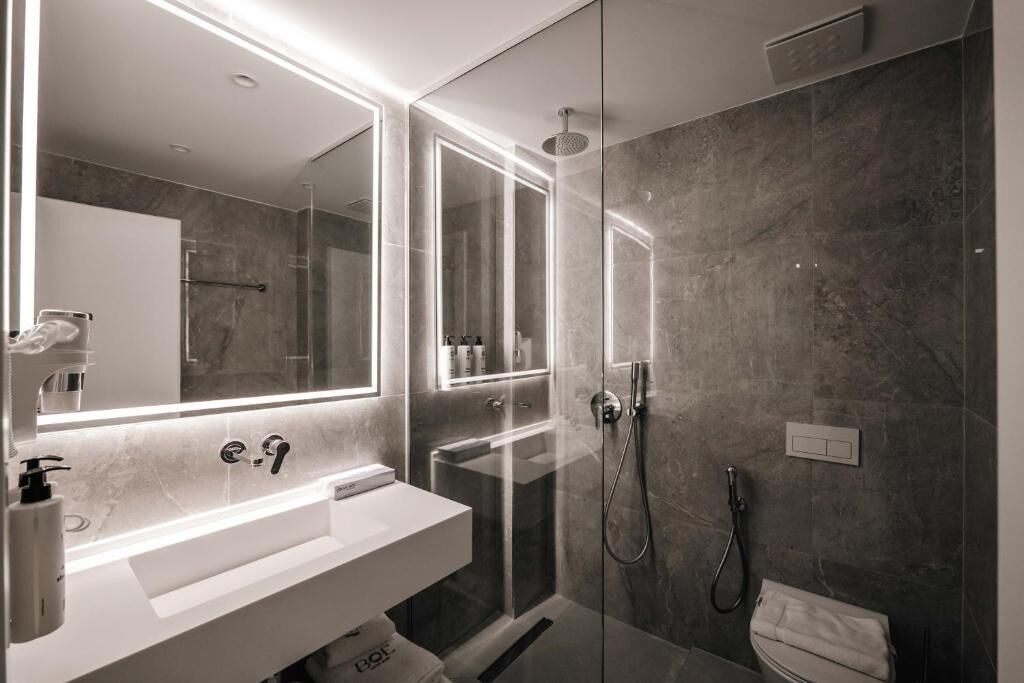 A modern bathroom with a glass-enclosed shower, a white sink, and a large mirror.