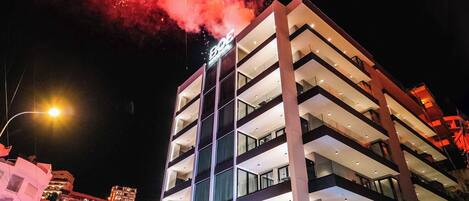 A multi-story hotel with a modern design, featuring balconies on each floor and a well-lit facade.