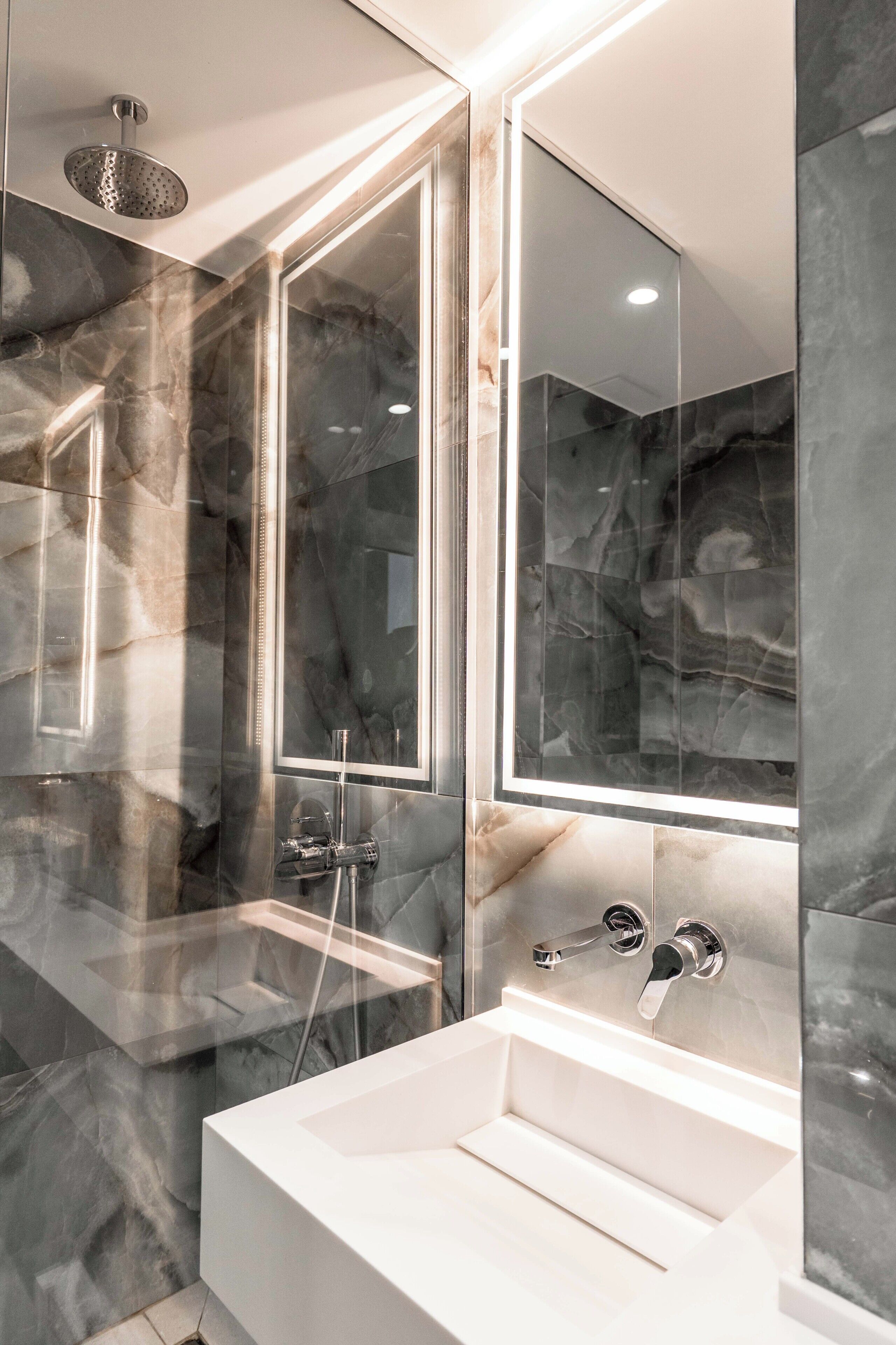 A modern bathroom with a glass-enclosed shower, a large mirror, and a white sink.