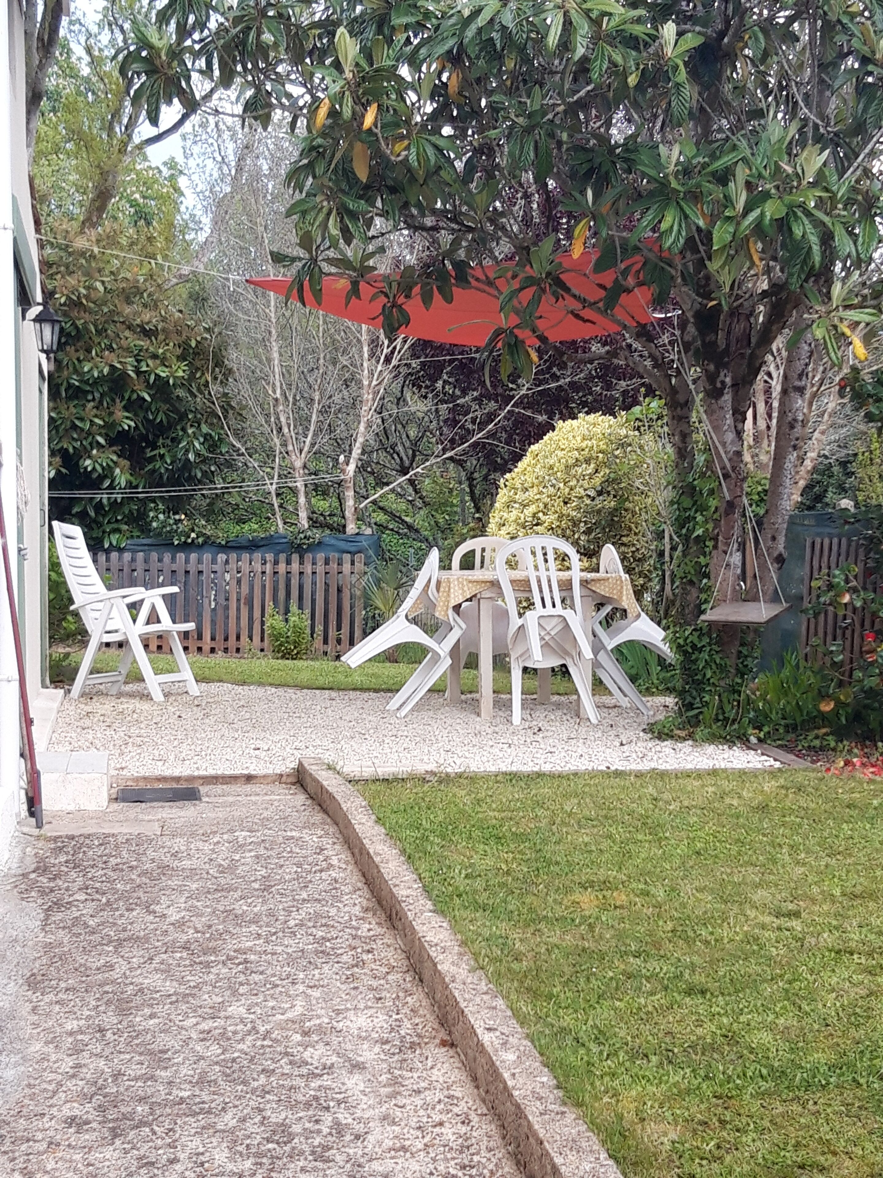Een terras met witte plastic stoelen en een tafel, omringd door een grindpad en een gazon.
