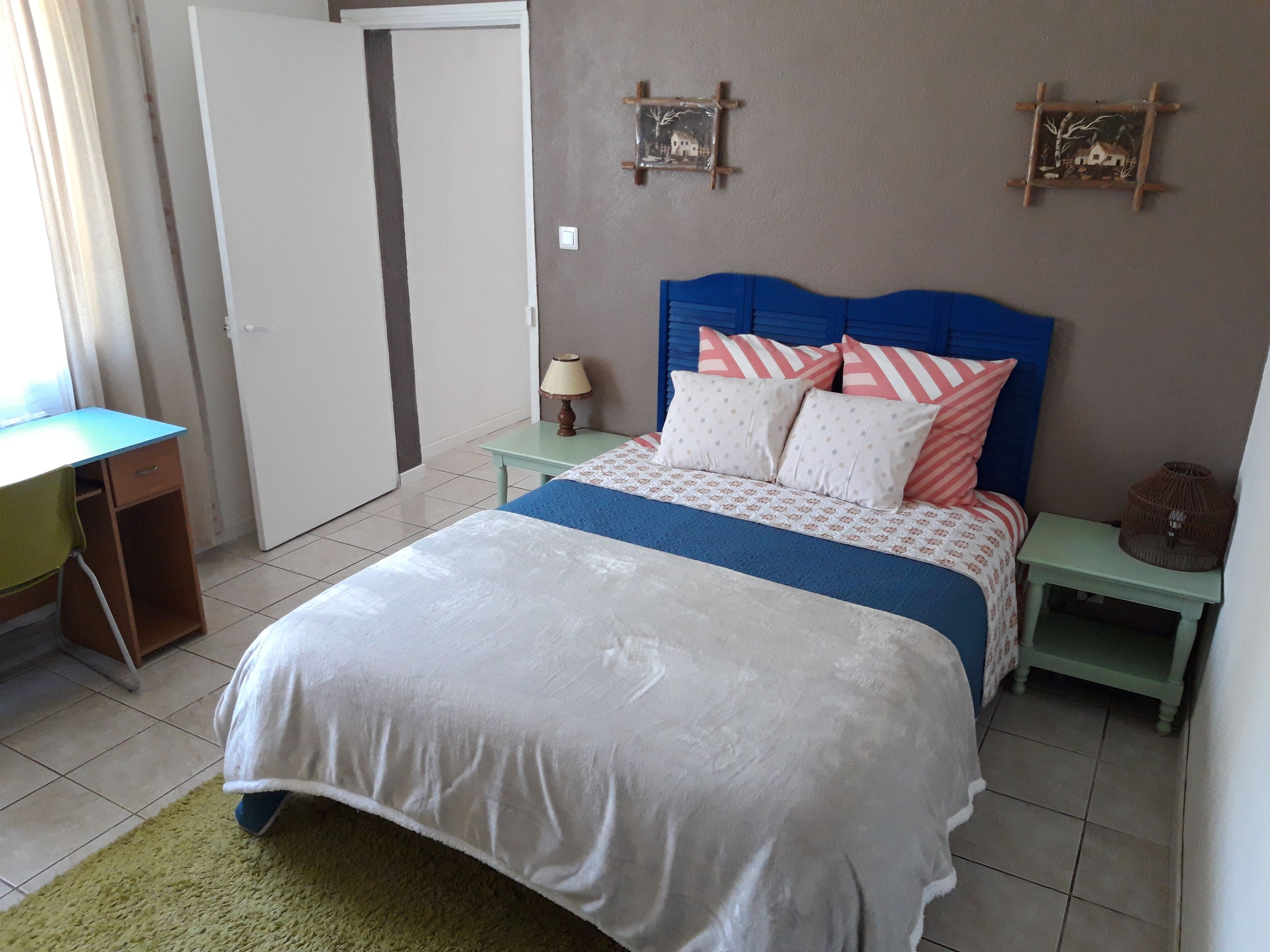 Un dormitorio con una cama, un escritorio y una silla. Se ve una puerta y un adorno en la pared.