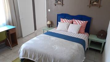 Un dormitorio con una cama, un escritorio y una silla. Se ve una puerta y un adorno en la pared.
