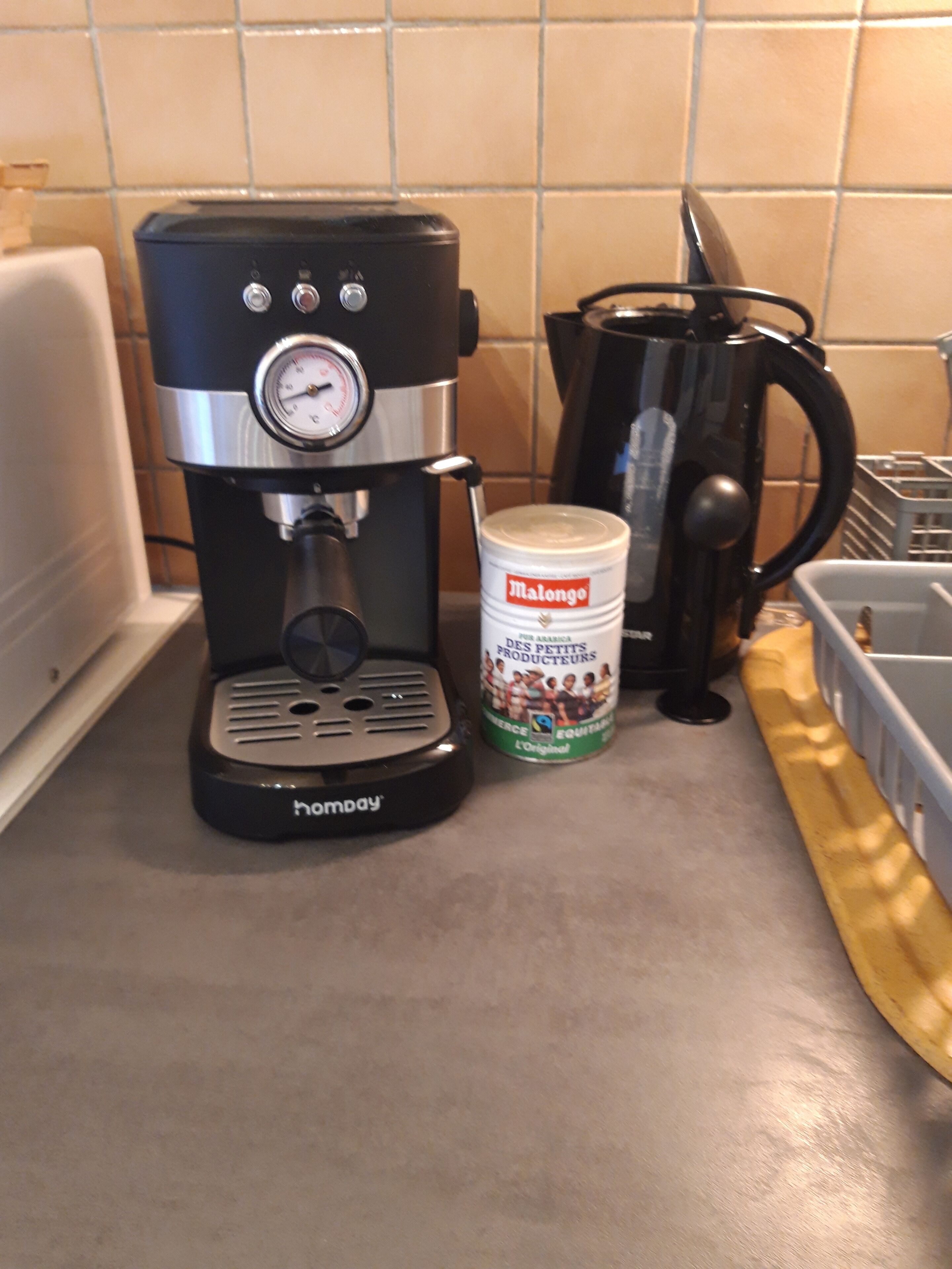 En kaffemaskine, en beholder med Malongo-kaffe og en sort kaffekande på en køkkenbordplade.