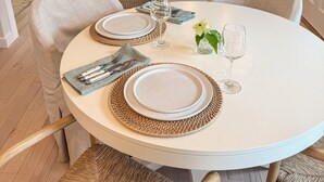 Un coin repas avec une table ronde dressée pour deux personnes, agrémentée de sets de table en fibres tressées et d’assiettes blanches.