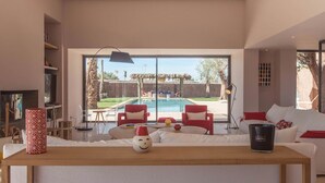 Ein modernes Wohnzimmer mit Blick auf einen Pool, einem Holztisch und roten sowie weißen Möbeln.
