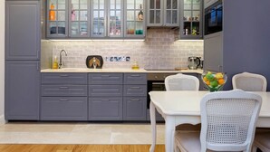 A modern kitchen with grey cabinets, a tiled backsplash, and a dining area with white chairs and a table. - The Westminster Courtyard Apartment, by Veeve (London)