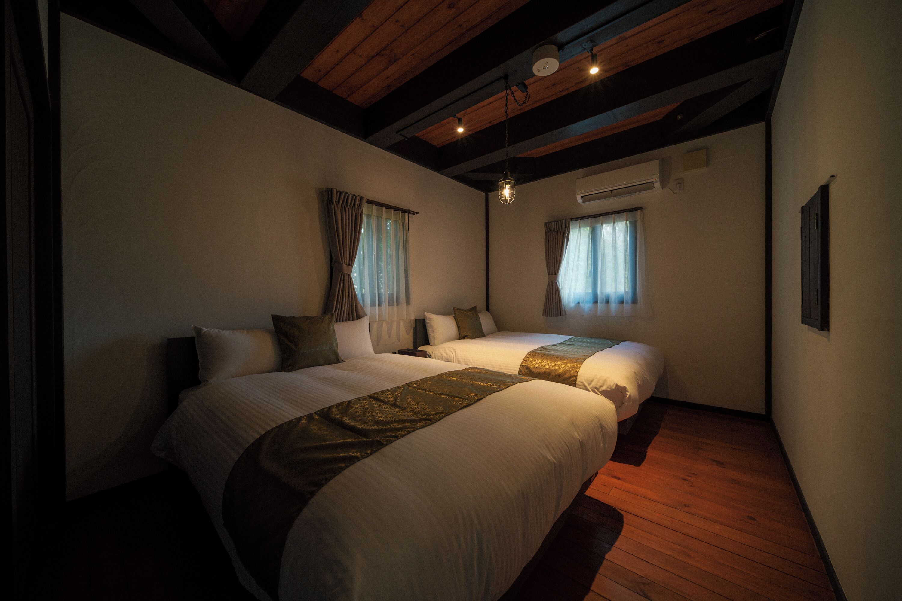 A hotel room with two beds, wooden flooring, and a sloped ceiling.