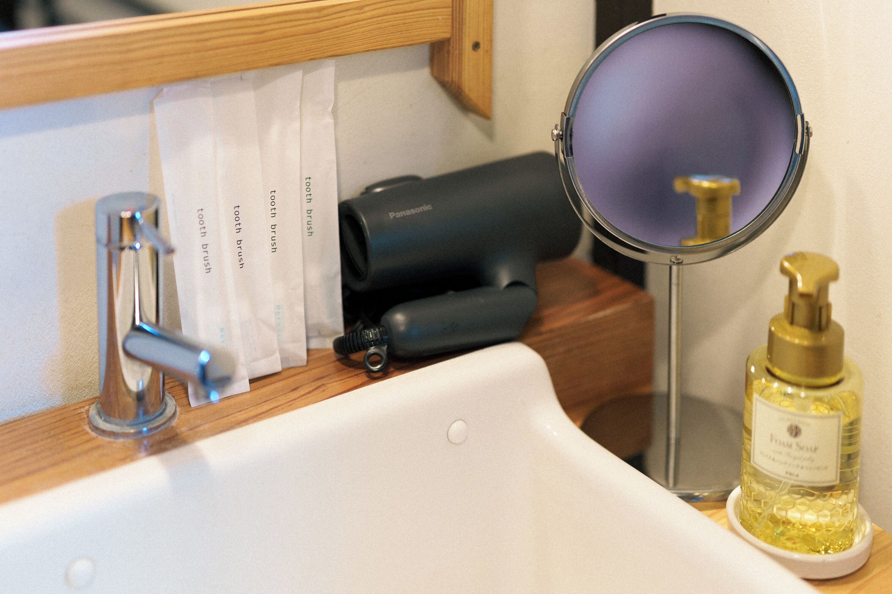 A bathroom sink with a faucet, a toothbrush holder, a mirror, and a bottle of hand soap.