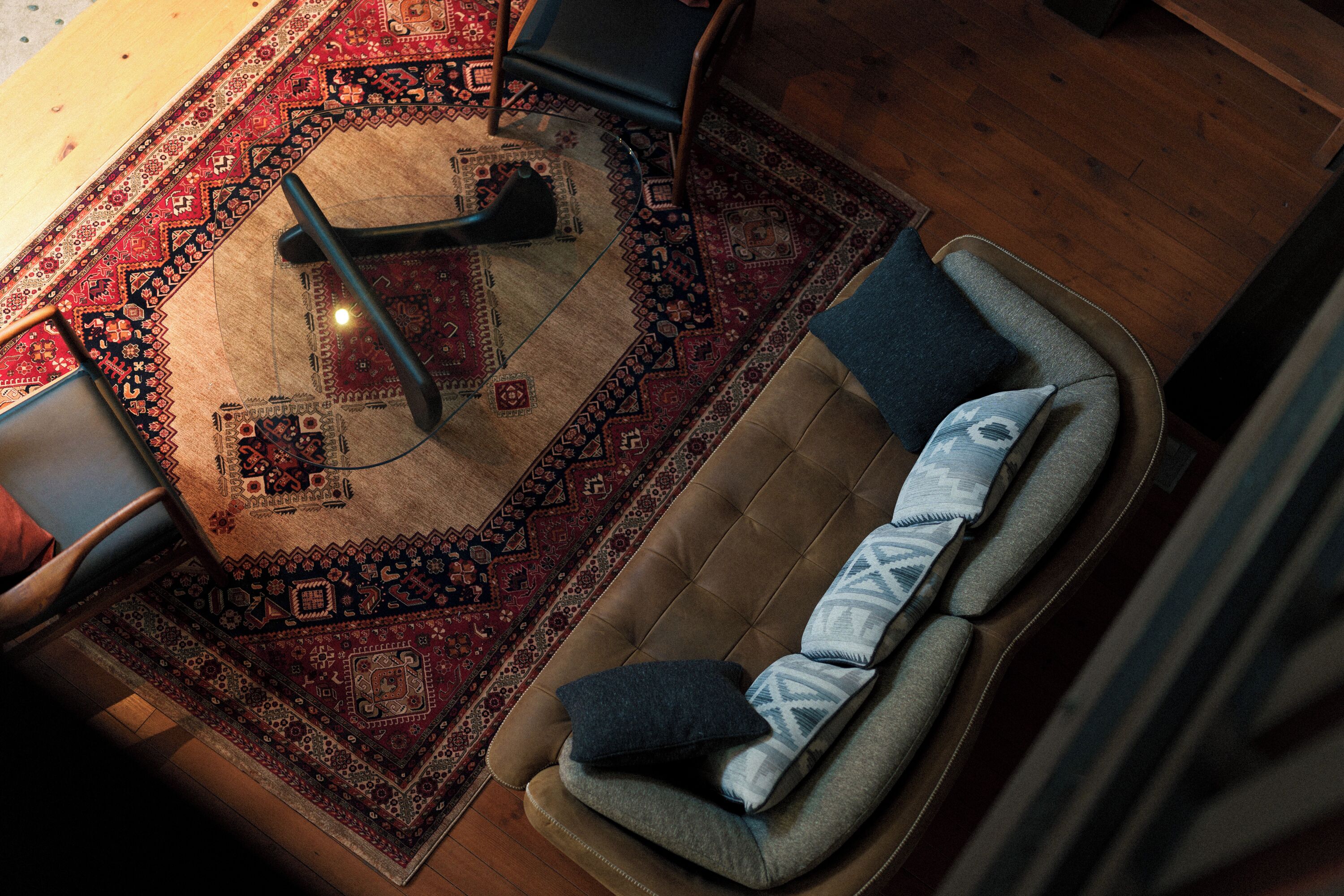 A living room with a brown sofa, a patterned rug, and a wooden floor.