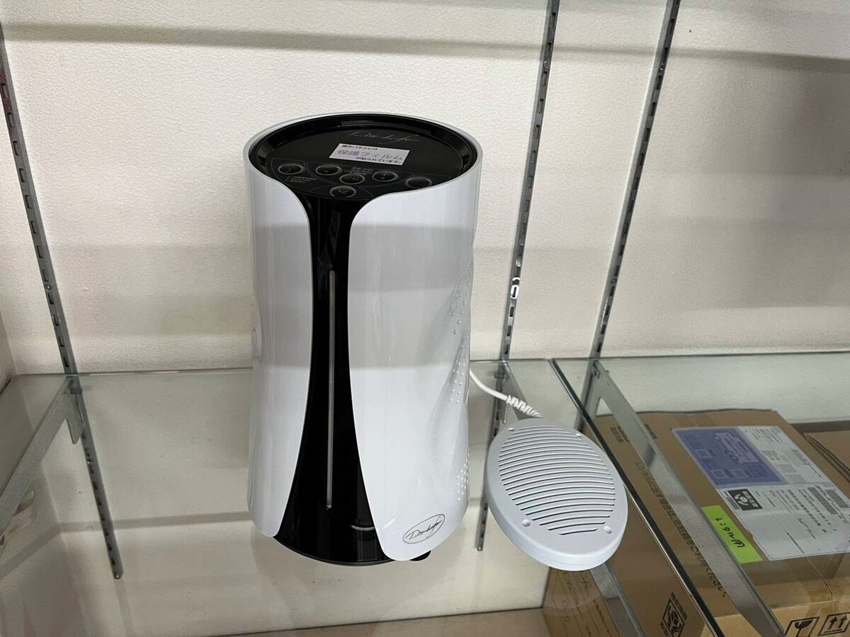 Un altavoz blanco y negro sobre una repisa de vidrio, con una caja de cartón al fondo.