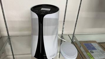 Un altavoz blanco y negro sobre una repisa de vidrio, con una caja de cartón al fondo.