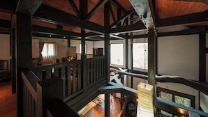 Un interior espacioso con techos altos y vigas de madera a la vista. Una escalera conduce a un nivel superior con vistas al exterior.