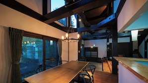 Un comedor con una mesa y sillas de madera, un candelabro y ventanas amplias con cortinas.