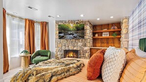 A cozy room with a stone fireplace, a green armchair, and a large fur throw. - Lux Nature Villa |Hot Tub + Theater + Games + Spa! (Fletcher)