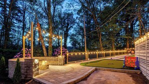 A landscaped outdoor area with a stone patio, a small fire feature, and a play area with a ball pit and a netted play structure. - Lux Nature Villa |Hot Tub + Theater + Games + Spa! (Fletcher)