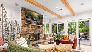 A spacious living room with a stone fireplace, comfortable seating, and large windows offering a view of the outdoors. - Lux Nature Villa |Hot Tub + Theater + Games + Spa! (Fletcher)