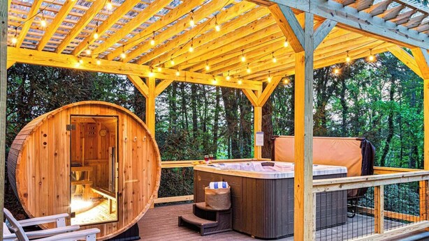 A wooden cabin with a hot tub and deck chairs, surrounded by trees. - Lux Nature Villa |Hot Tub + Theater + Games + Spa! (Fletcher)