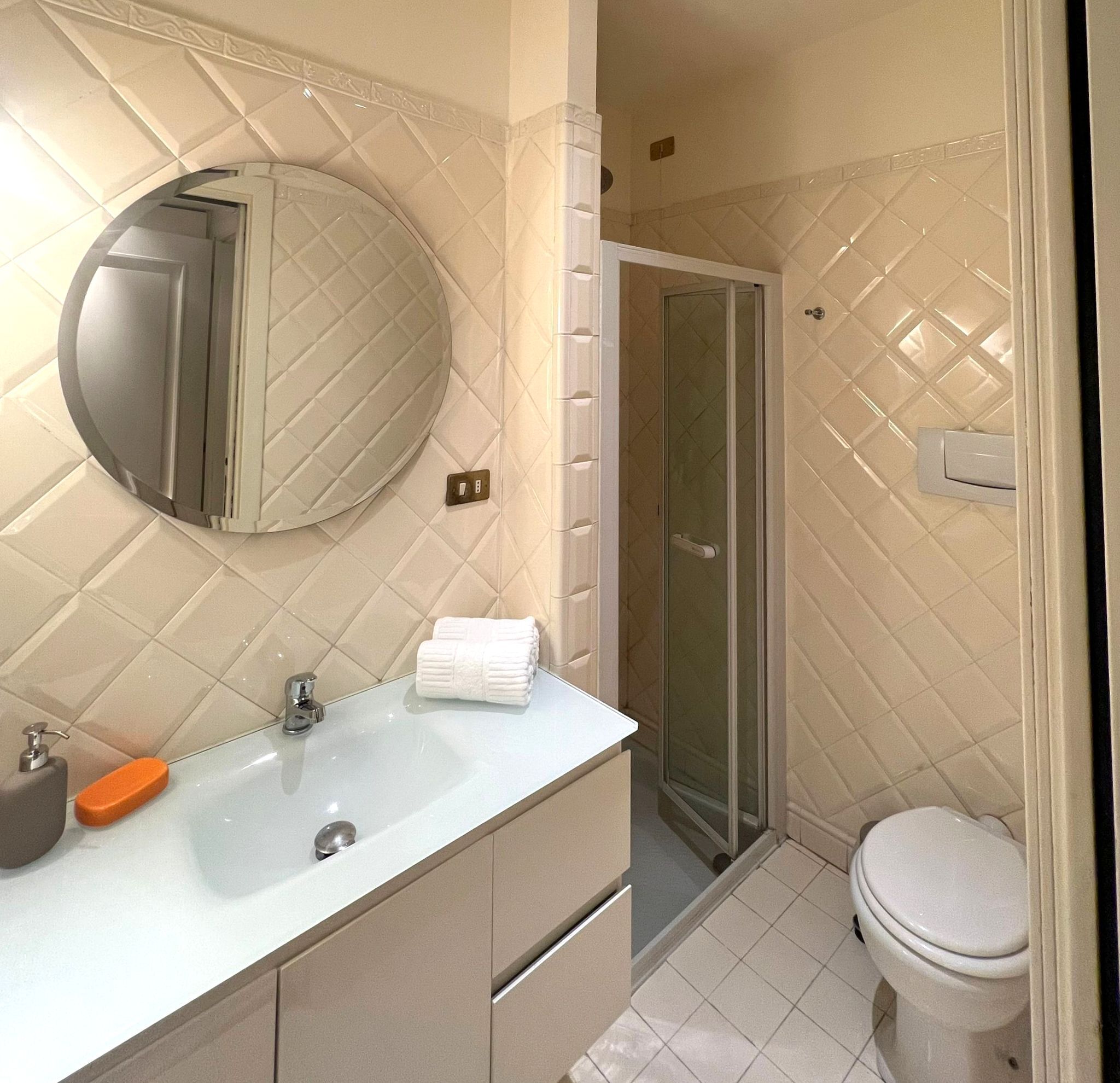 A bathroom with a white sink, mirror, and toilet. There is a glass shower door and a towel on the sink.