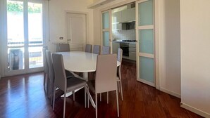 A spacious dining area with a round table and chairs, a kitchen visible through frosted glass doors, and a wooden floor.