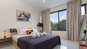 Ein modernes Schlafzimmer mit einem großen Bett, einem Nachttisch, einem Beistelltisch, einem Wandbild und einem Fenster mit Vorhängen.