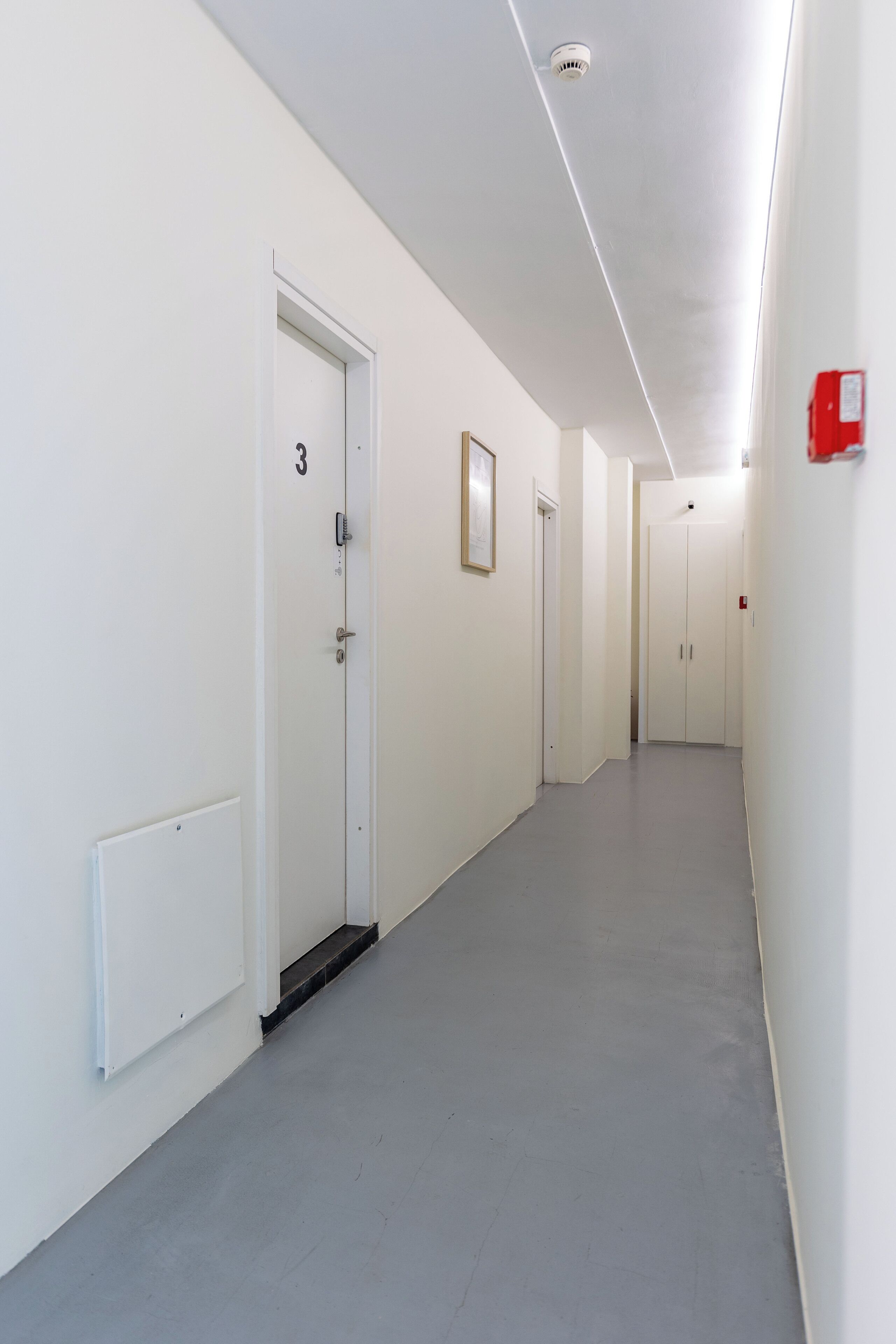 A hallway with white walls, grey flooring, and doors numbered 3 and 4.
