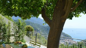 A balcony with a table set for two, a bench, and a view of the sea and hills. - Old Farmhouse "Green Apt",trekking lovers vacation homes with splendid views (Ravello)