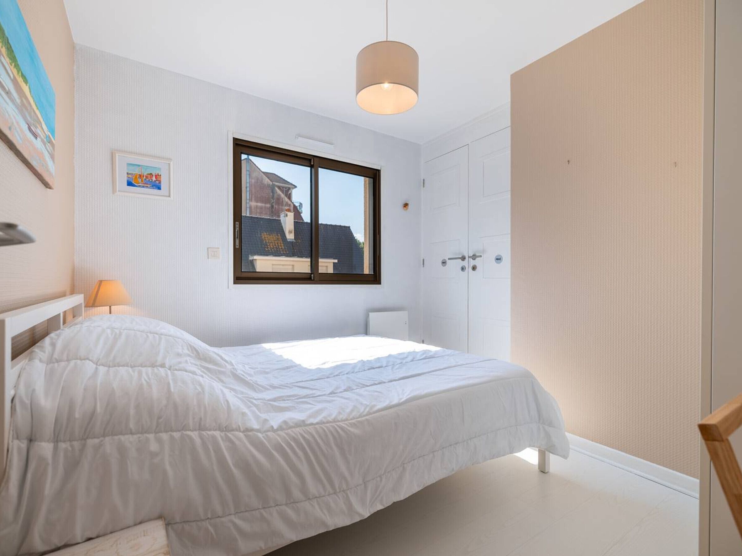A bedroom with a bed, a window, a door, and a lamp.