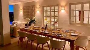 Un comedor con una larga mesa de madera dispuesta para una comida, rodeado de sillas blancas.