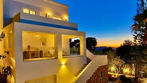Una casa moderna de varios niveles con una escalera que lleva al piso superior, ventanas amplias e iluminación exterior.