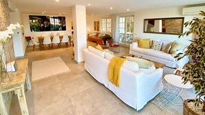 Un amplio espacio de sala con un sofá blanco, una mesa de comedor con sillas, y una cocina al fondo.