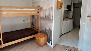 A compact room with a bunk bed, a small wooden stool, a kitchen area with a microwave, and a door leading to another room. - Renovated studio in Avoriaz center, perfect for 4 guests (Avoriaz)