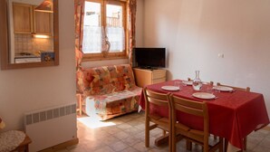 A cozy dining area with a red table, wooden chairs, and a television on a small table. - Cozy apartment in Aussois for 3/4 guests, near shuttles (Aussois)