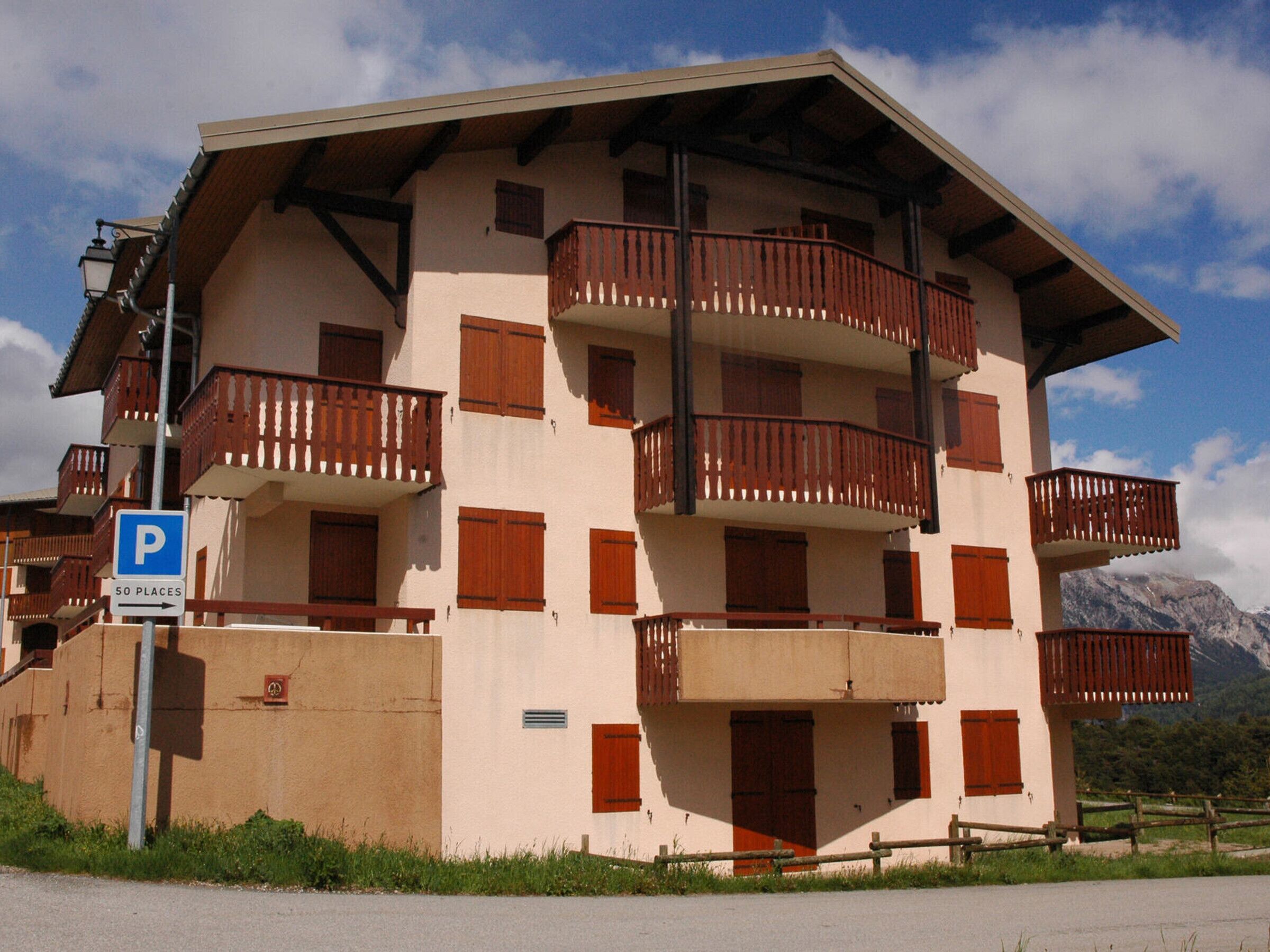A multi-story building with balconies, a parking sign, and a mountainous backdrop.