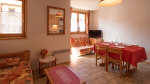 A cozy living room with a sofa, a small table, a dining table with chairs, a television, and a window with curtains. - Cozy apartment in Aussois for 3/4 guests, near shuttles (Aussois)