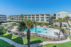 Ein Hotel mit Schwimmbad, umgeben von einem Zaun, Palmen und einem gepflegten Rasen.
