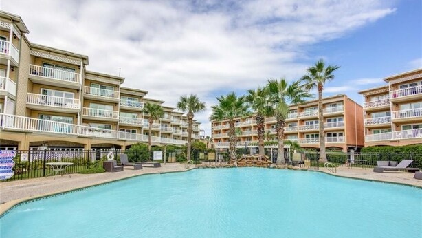 A hotel with a large swimming pool surrounded by palm trees and multiple balconies. - Sandy Shores - Babe's Beach / Welcomes 8 (Galveston)
