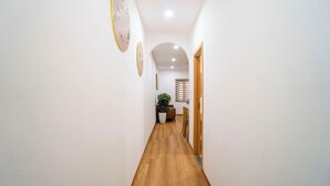 Un estrecho pasillo con suelo de madera, paredes blancas y una puerta que da a un comedor con mesa y sillas.