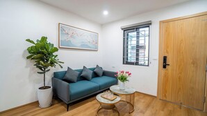 Una sala de estar con un sofá color turquesa, una planta en maceta, una mesita redonda con un jarrón de flores y una puerta de madera.