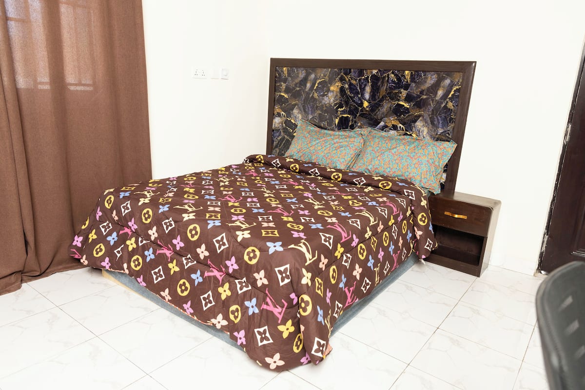 Uma cama com colcha estampada, cabeceira com design que lembra mármore e mesa de cabeceira com gaveta.
