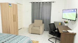 A room with a bed, a desk with a computer, a chair, a TV, and a wardrobe.