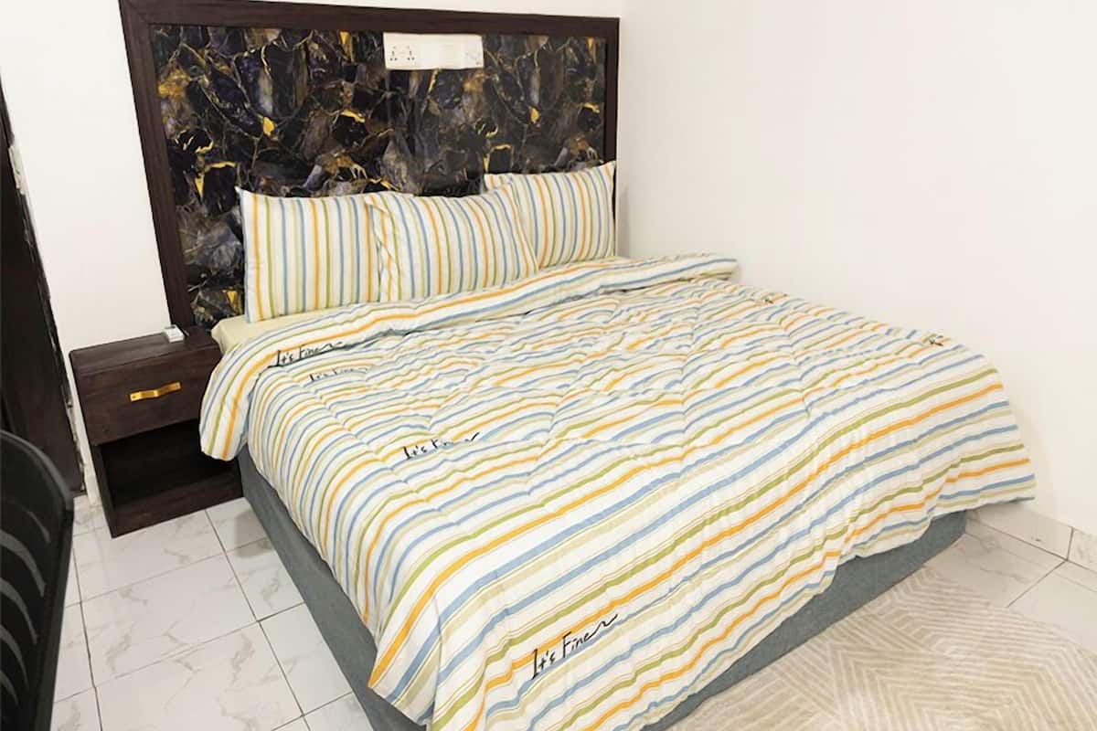 Quarto com colcha listrada, cabeceira escura e mesa de cabeceira com gaveta.