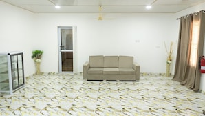 A room with a beige sofa, a ceiling fan, a patterned floor, a door, and a fire extinguisher.
